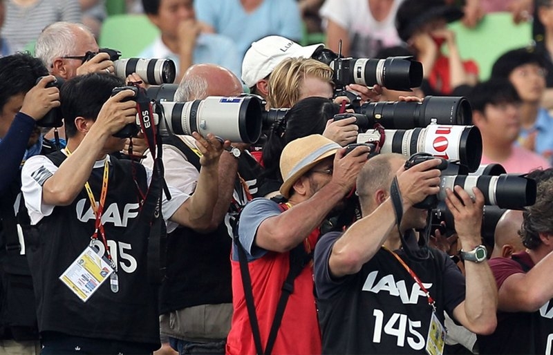 Image of a group of photographers capturing live sport action beside audiences. 